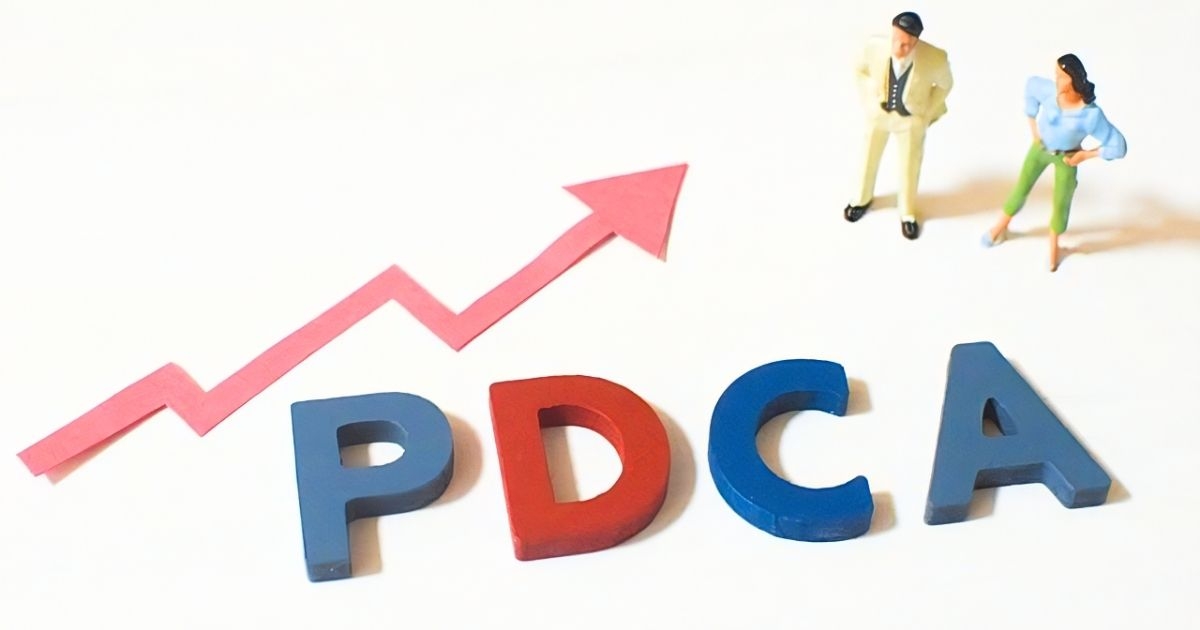 PDCAの文字と上向き矢印を眺めるミニチュア