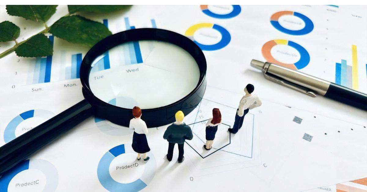 グラフの上に置かれた虫眼鏡を眺めるミニチュア